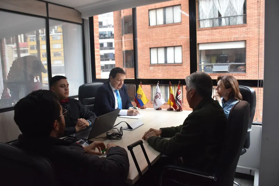 Reunión de asesoría en la sala de juntas de Grupo Greco Abogados, con bandera de Colombia